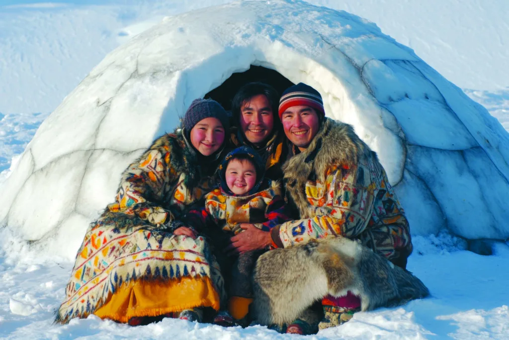 Eskimo or Inuit Family Dressed in Traditional Arctic Clothing Poses Near Their Snowy Home Igloo
