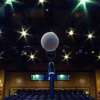 A microphone on a lit stage at Cranleigh Arts Centre, looking out over rows of empty seats