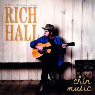Comedy poster showing a performer seated with an acoustic guitar against weathered wooden boards