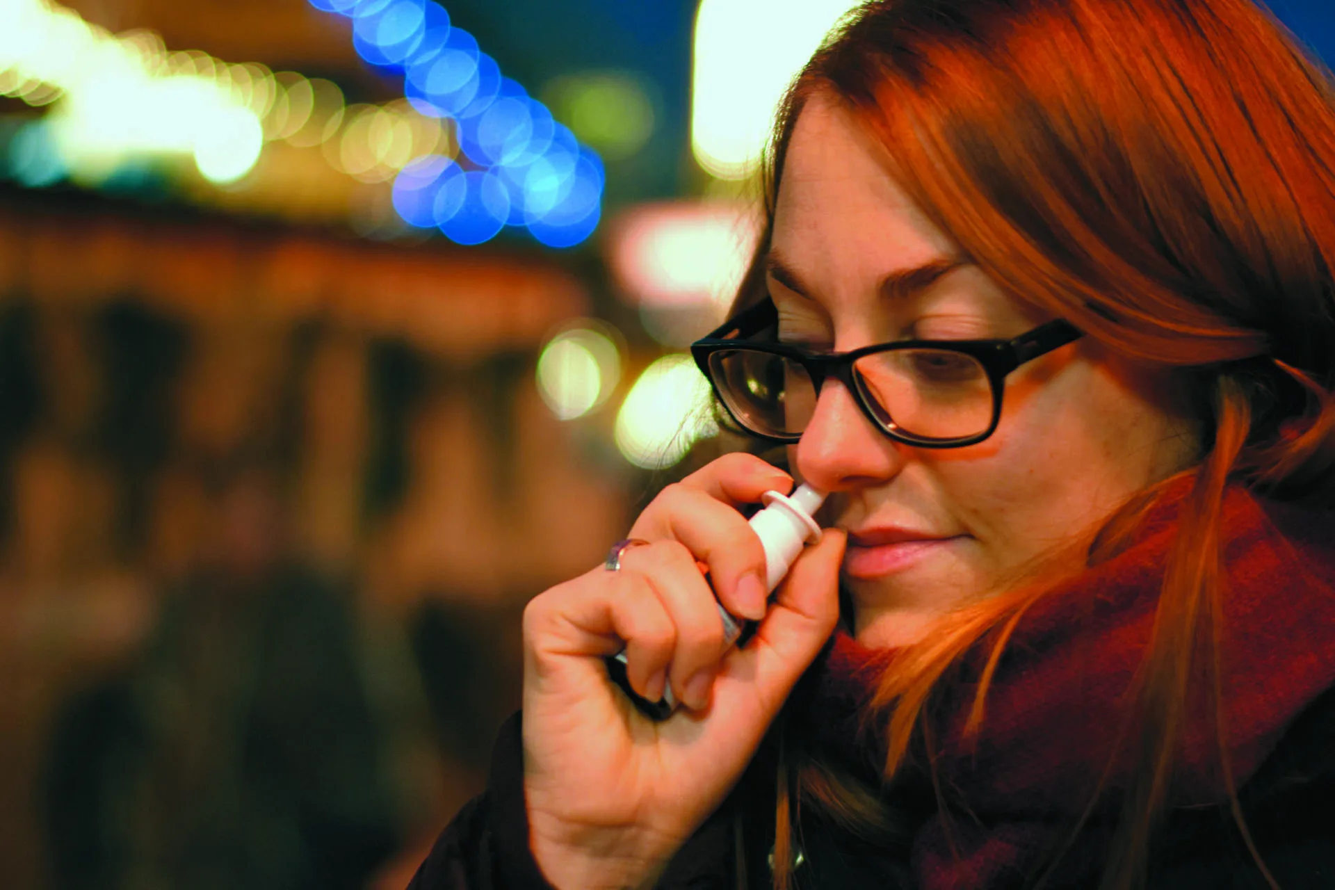 A woman using a saline nasal spray outdoors