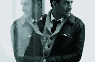 Andrew Gow, portrait painter, photographed in a leather jacket beside a reflective window