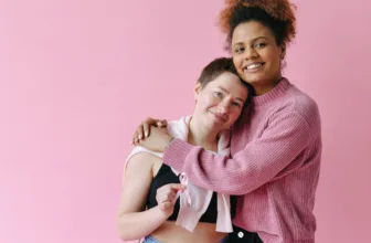 Two smiling women hugging against a pink background