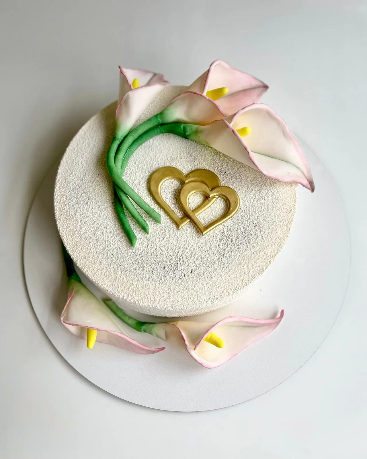 A white cake decorated with pink calla lilies and two gold hearts
