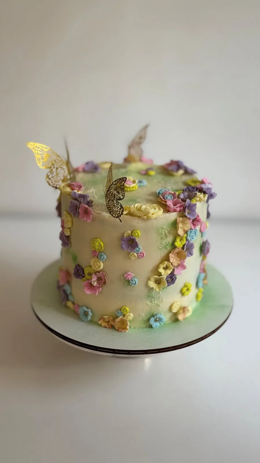 A tall celebration cake decorated with small piped flowers and gold butterflies
