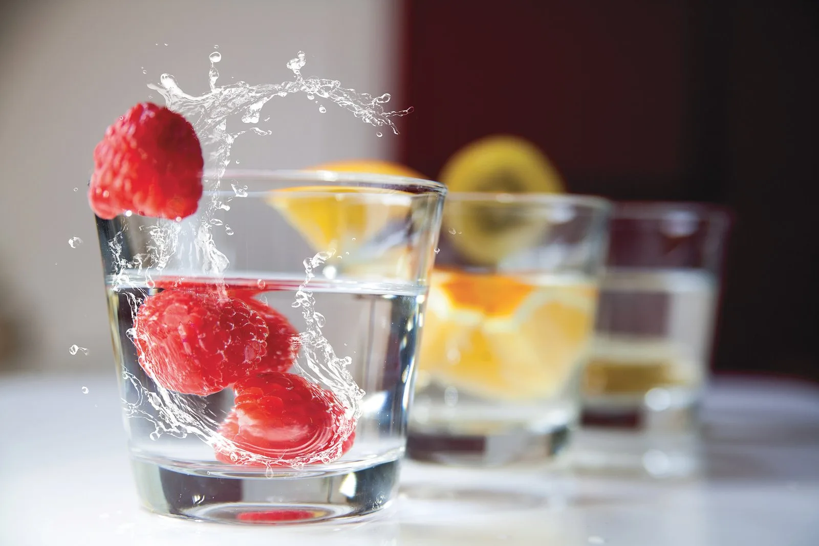 Glasses of water with strawberries and citrus slices splashing into them