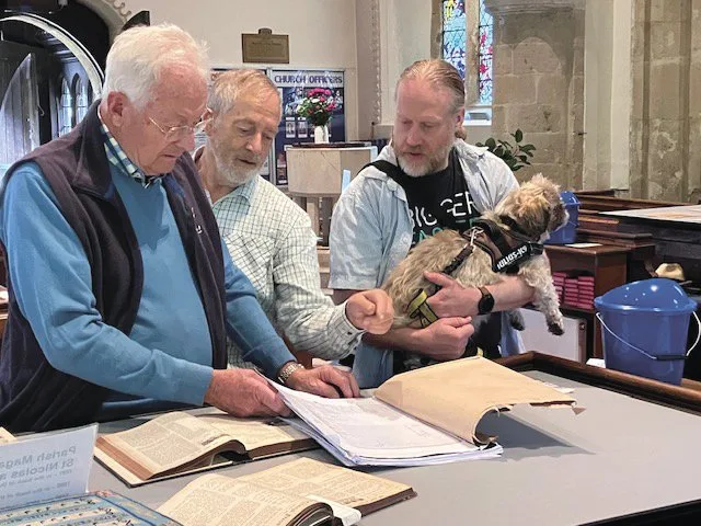 Three men studying old record books spread out on a table inside the church