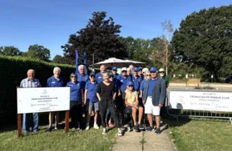 Members of Cranleigh Pétanque Club in blue club shirts, gathered outdoors with Lynn Murray beside two banners