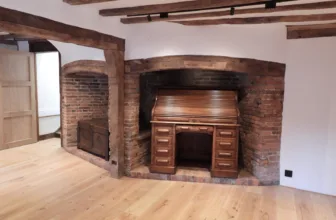 A restored brick inglenook fireplace with a wooden roll top desk in front of it, in the Napper Centre