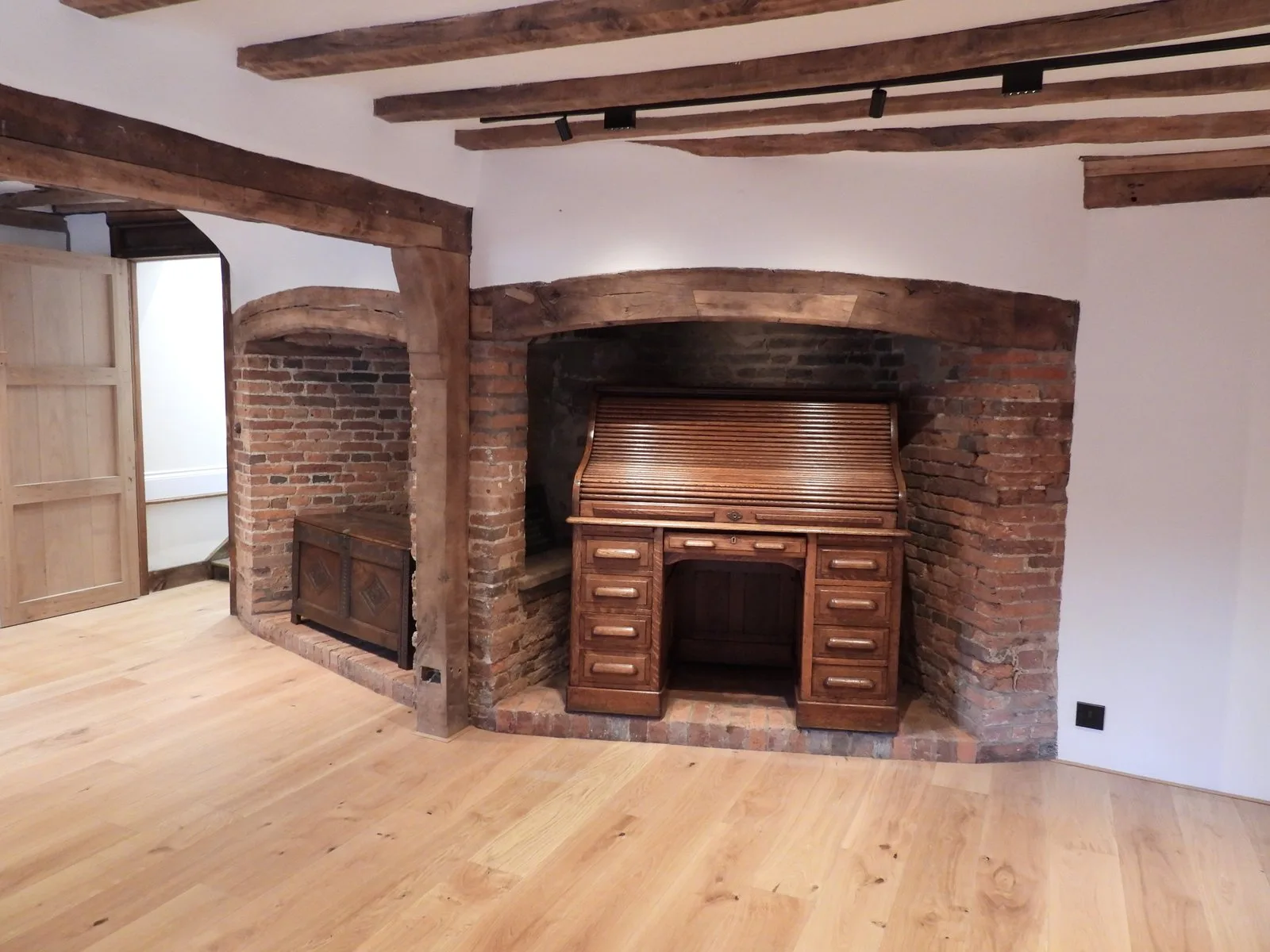 A restored brick inglenook fireplace with a wooden roll top desk in front of it, in the Napper Centre