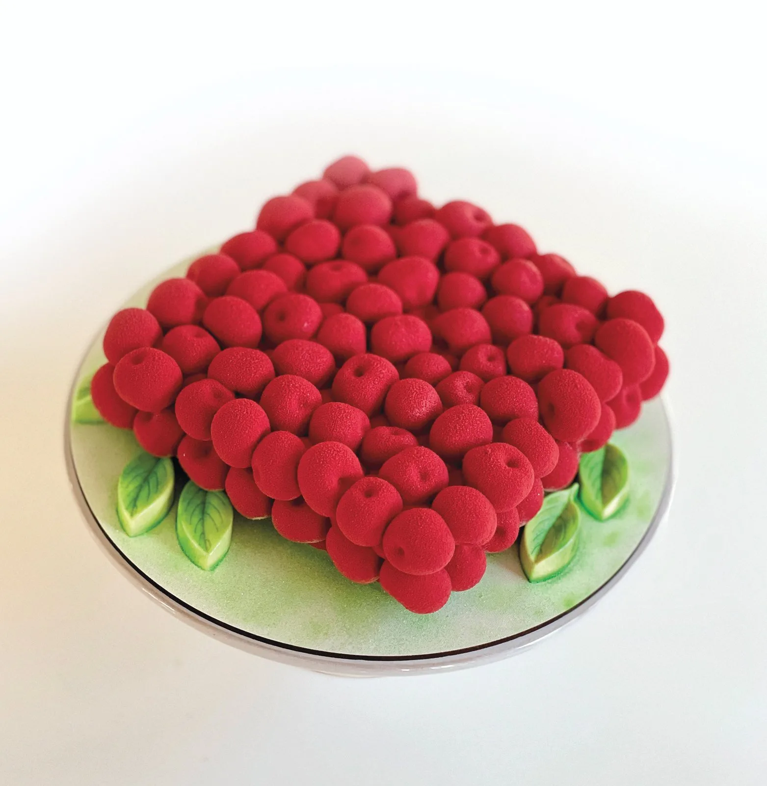 A square cake covered in small round red berries, with green leaves at the corners